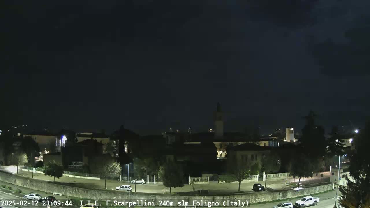 A nighttime view of a town with a few cars on the roads under a dark, cloudy sky.