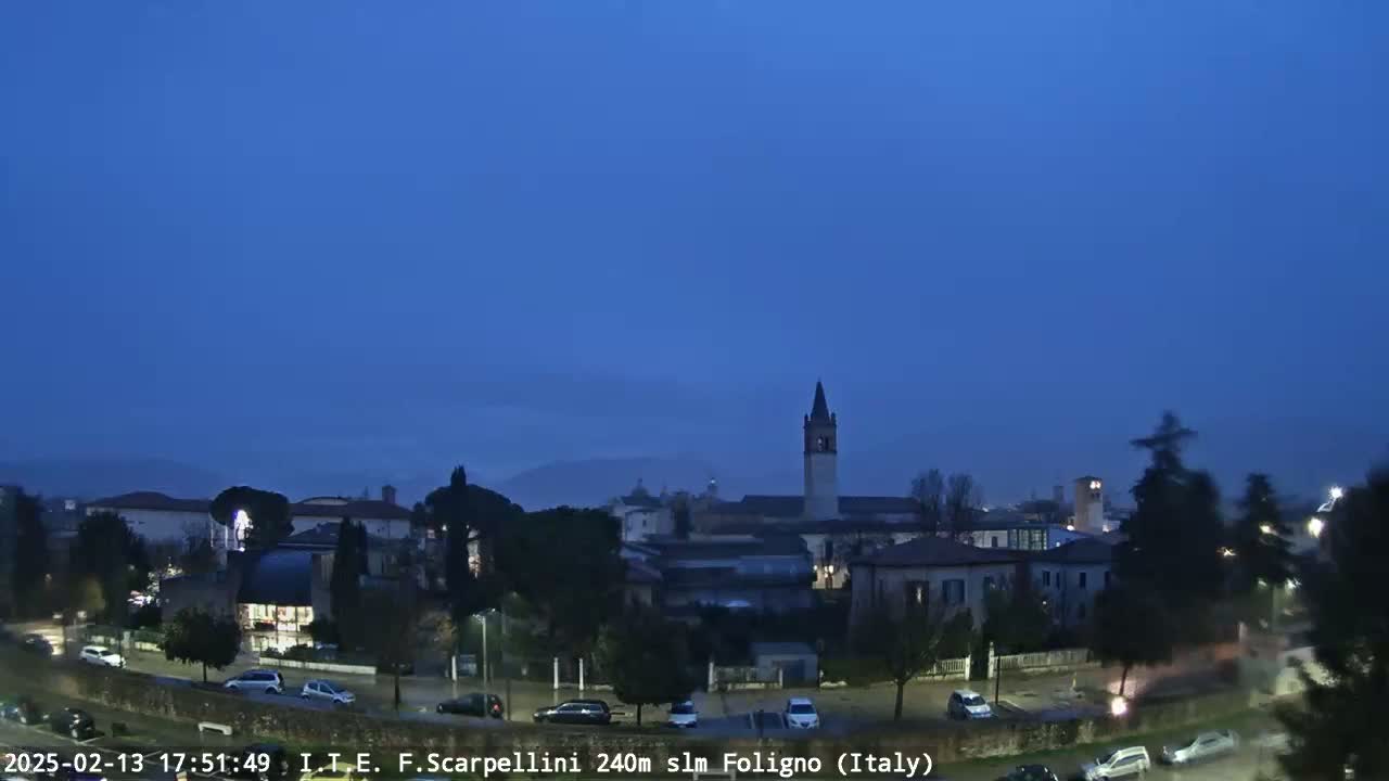 A twilight view of a town with a tall bell tower, under a clear, dark blue sky.