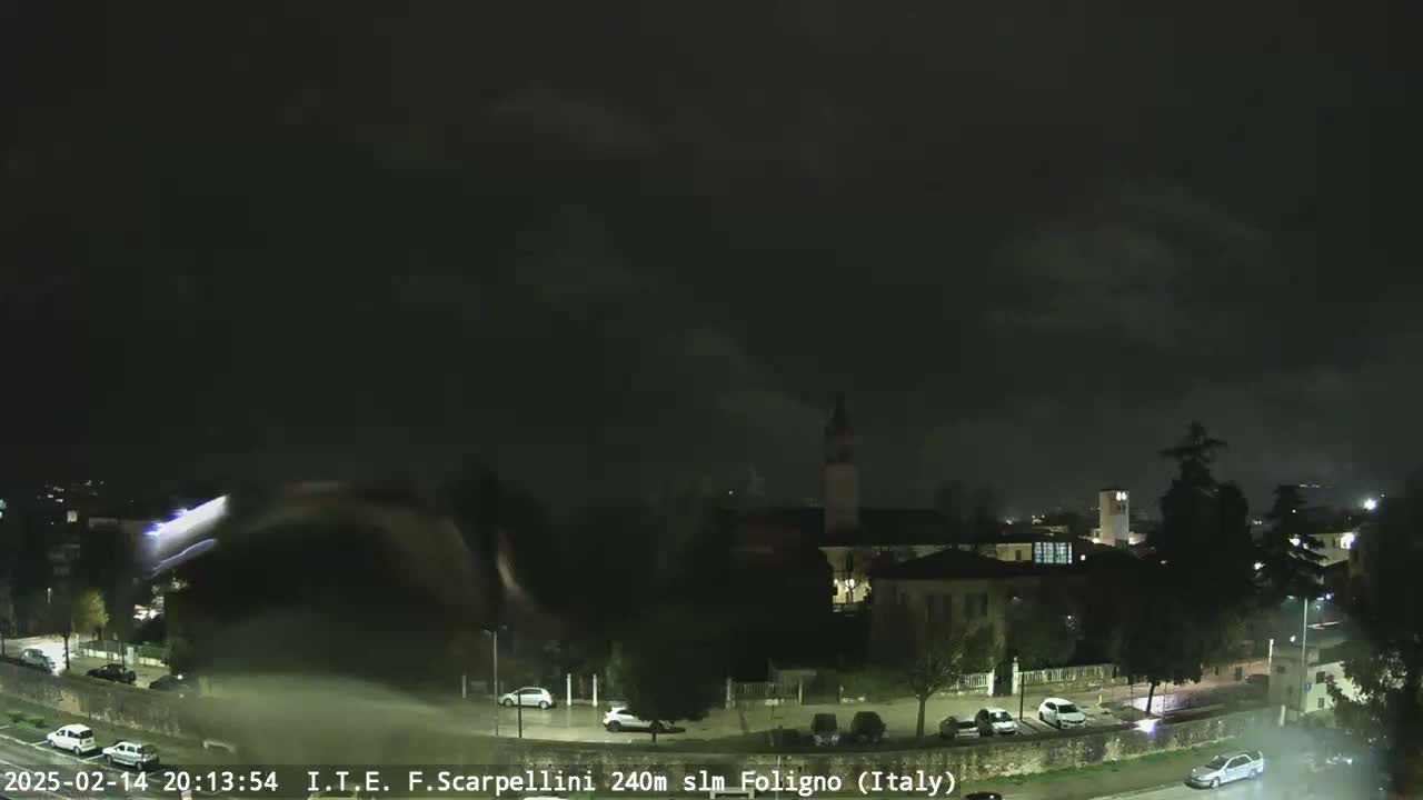 A nighttime view of a town under a dark, cloudy sky with rain falling.