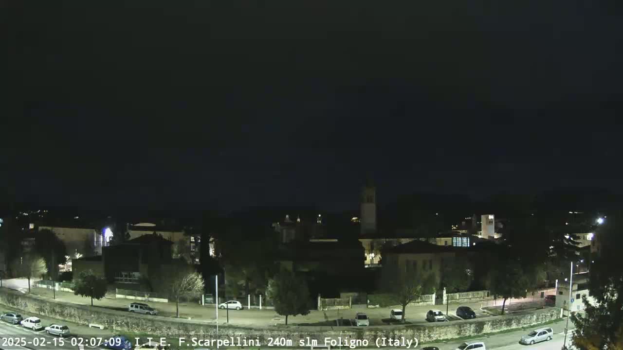 A nighttime view of a town with buildings and parked cars under a dark, clear sky.