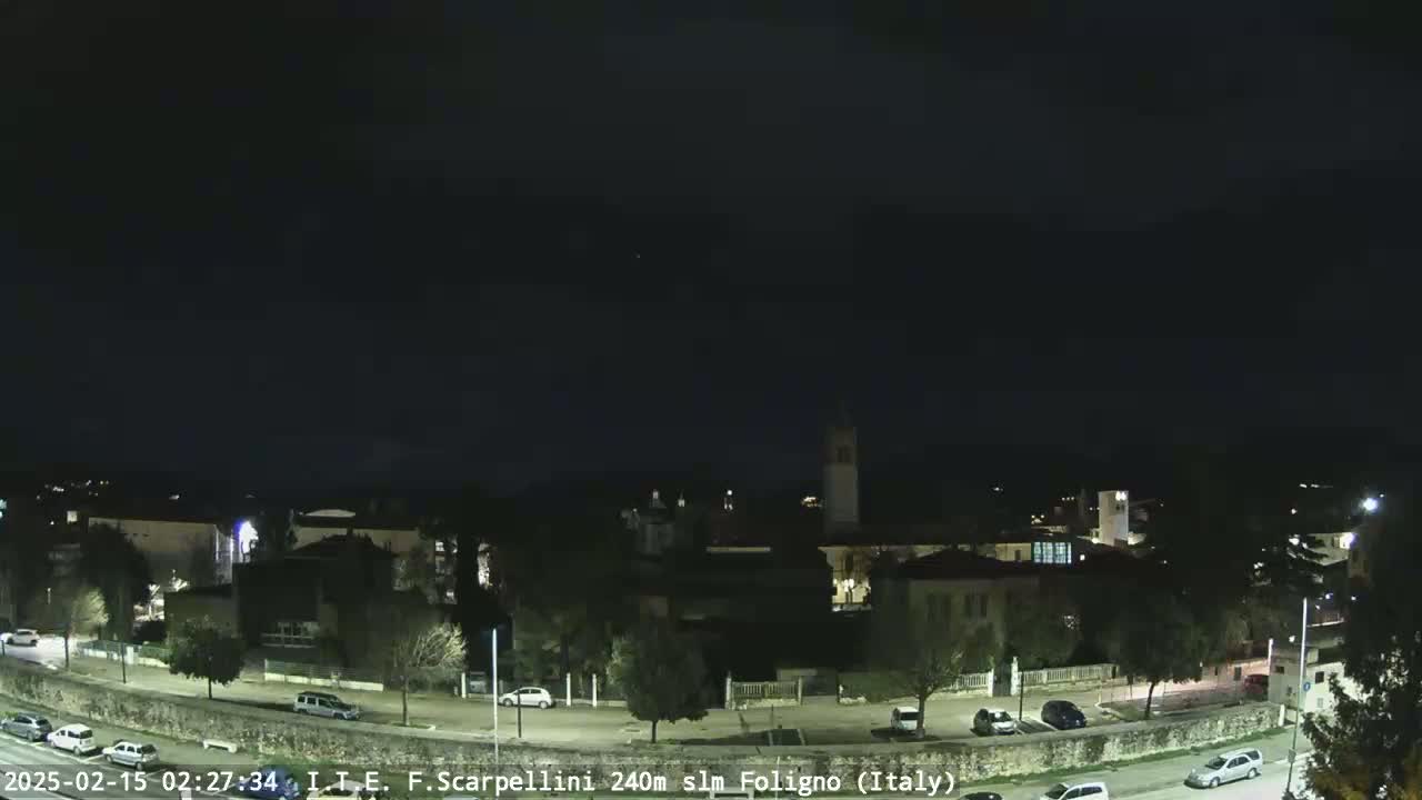 A nighttime view of a town with buildings and parked cars under a dark, clear sky.
