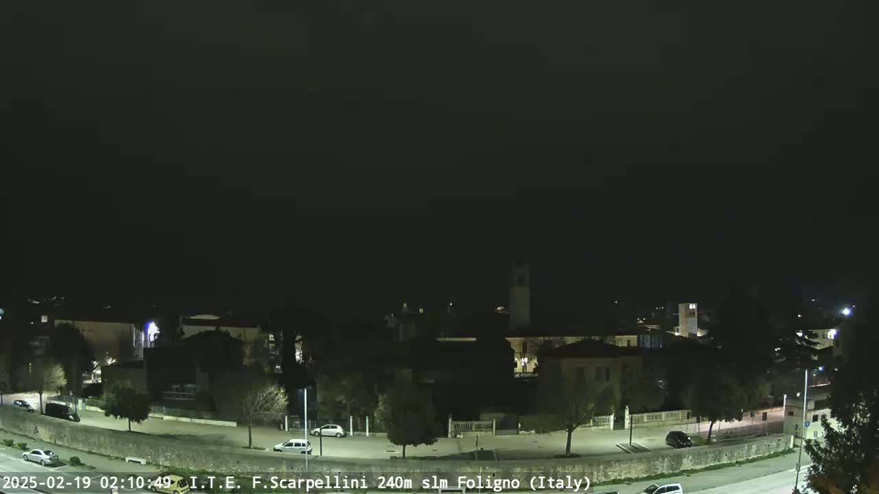 A nighttime, dimly lit view of a town with a few cars on the roads, under a dark, clear sky.