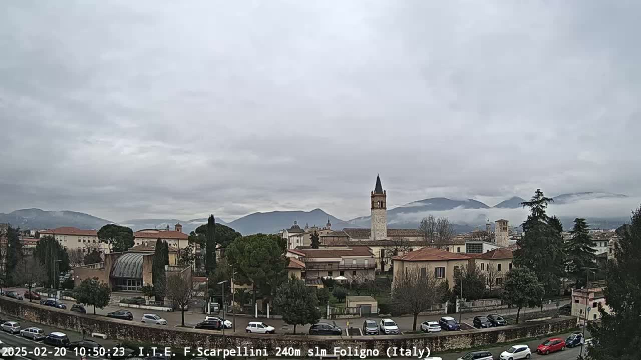 A town in a valley, under a cloudy sky, with mountains shrouded in fog in the background.