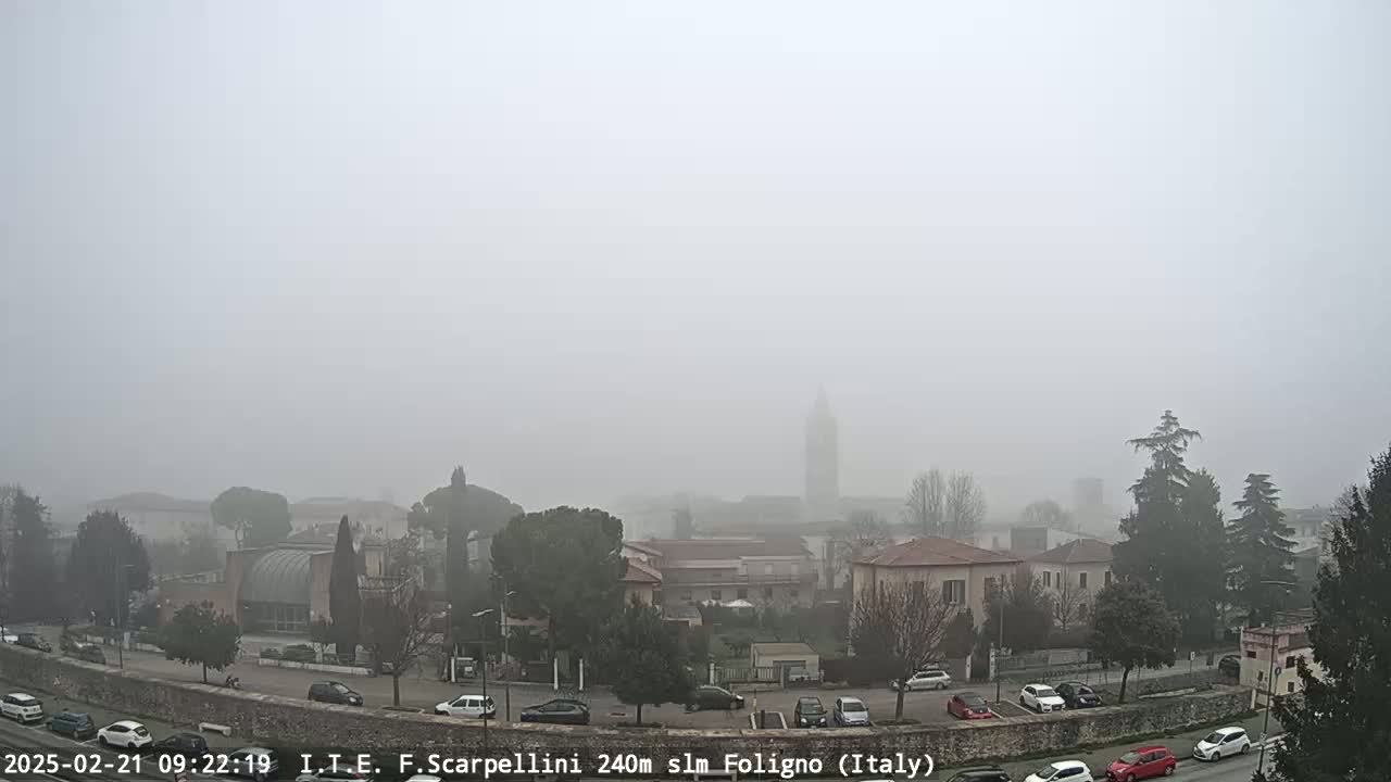 A foggy view of a town with buildings, cars in a parking lot, and trees.