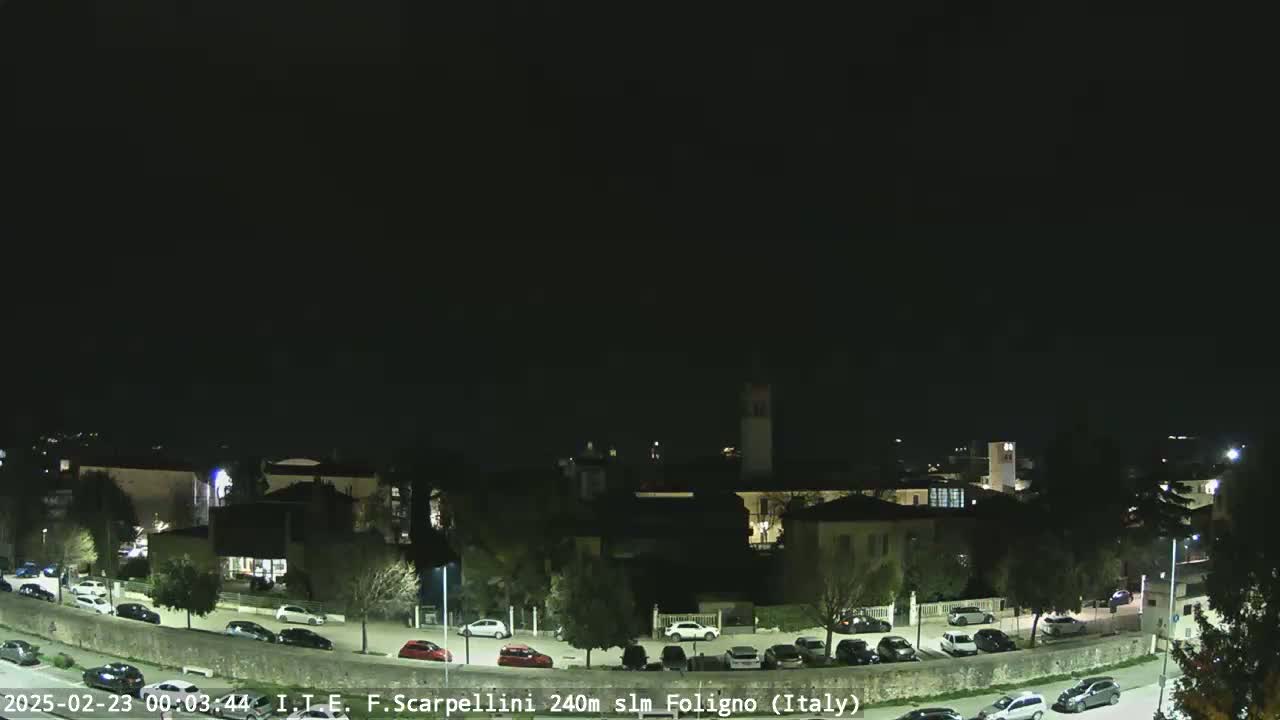 A nighttime view of a town with parked cars and buildings under a clear, dark sky.