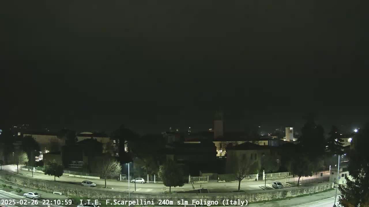A nighttime, dimly lit view of a town with a road curving through it under a dark, overcast sky.