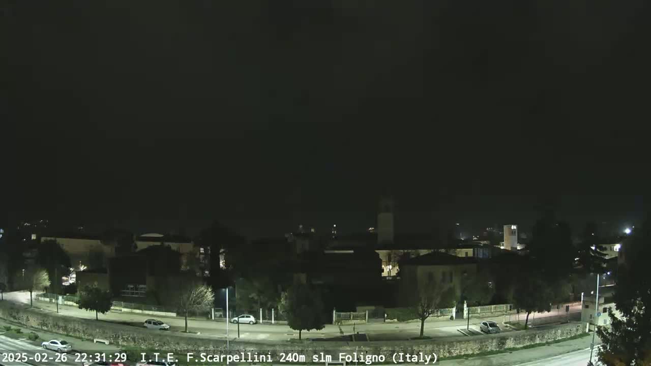 A nighttime, long shot of a town with a few cars on the road, under a clear, dark sky.