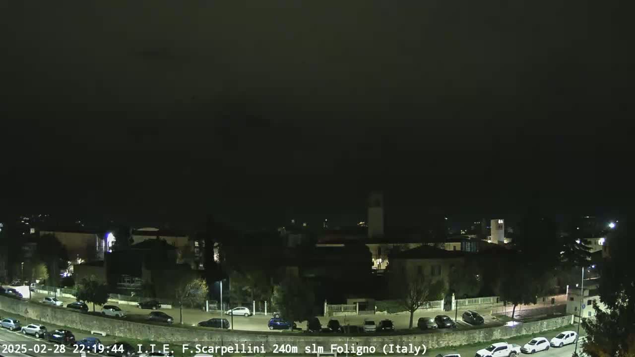 A nighttime view of a town with parked cars along a street, under a dark, overcast sky.