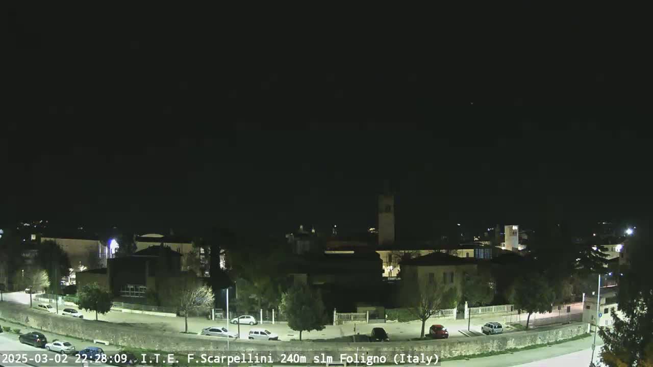 A nighttime view of a town with a few cars parked along a curved road under a clear, dark sky.
