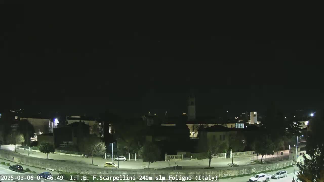 A nighttime view of a town with a few cars parked along a road, under a clear, dark sky.