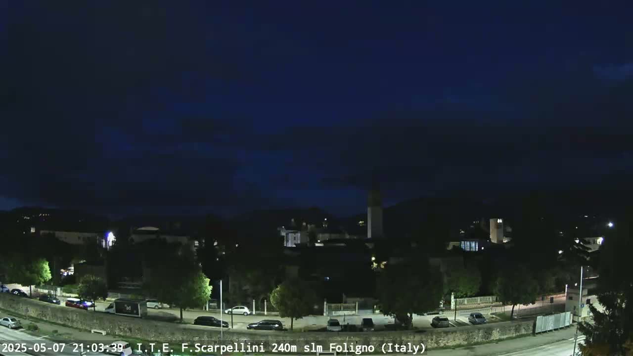 A nighttime view of a town with cars parked along a road under a dark, clear sky.