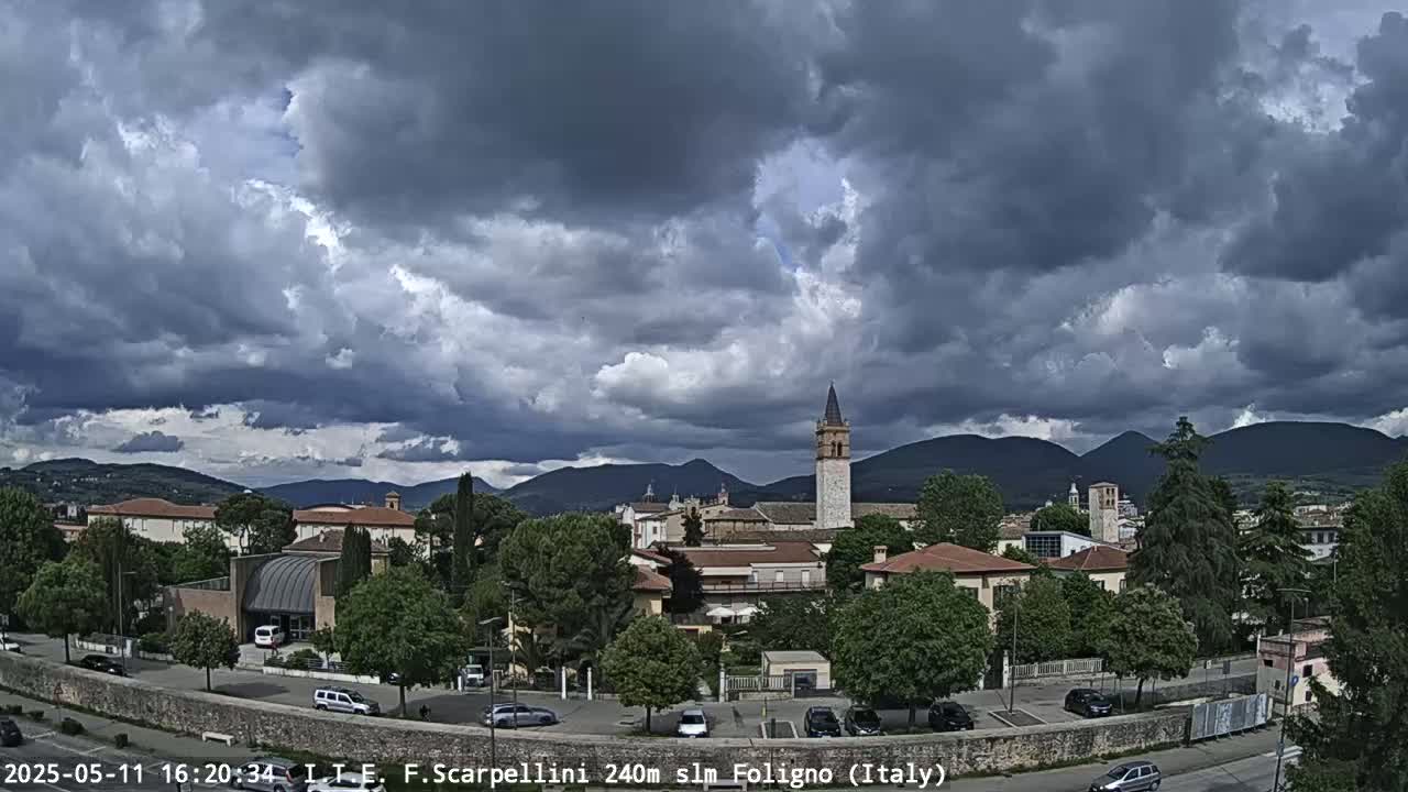 A town nestled in a valley under a heavily clouded sky, with mountains in the distance.