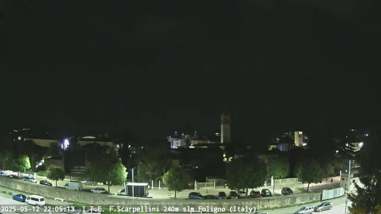 A nighttime view of a town with parked cars and a few streetlights, under a clear, dark sky.
