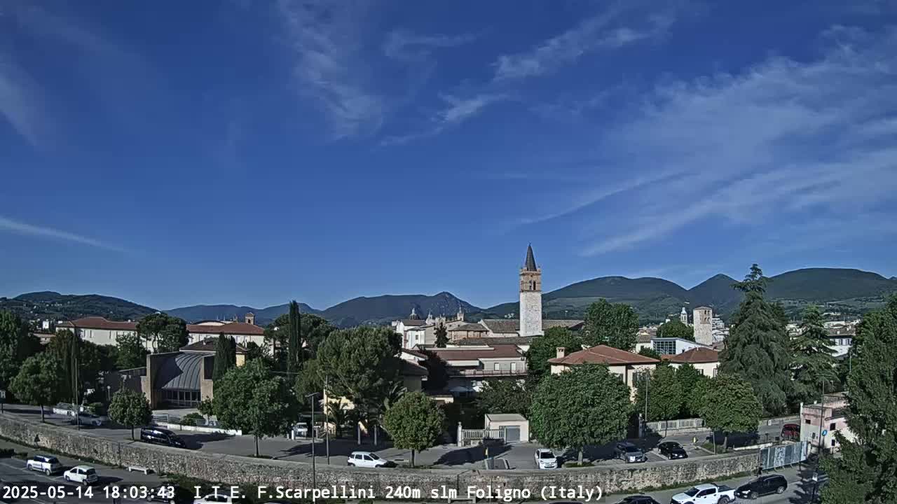 Under a clear blue sky, a town with buildings and a tall tower is nestled among green hills.