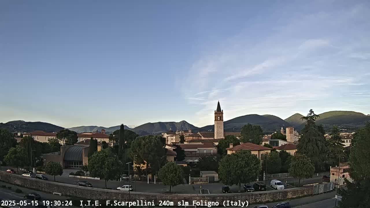 A clear evening view of a town nestled in a valley, surrounded by mountains under a pale blue sky.