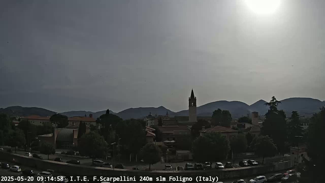 A hazy, sunny day reveals a town nestled among hills, with a tall bell tower as a prominent feature.
