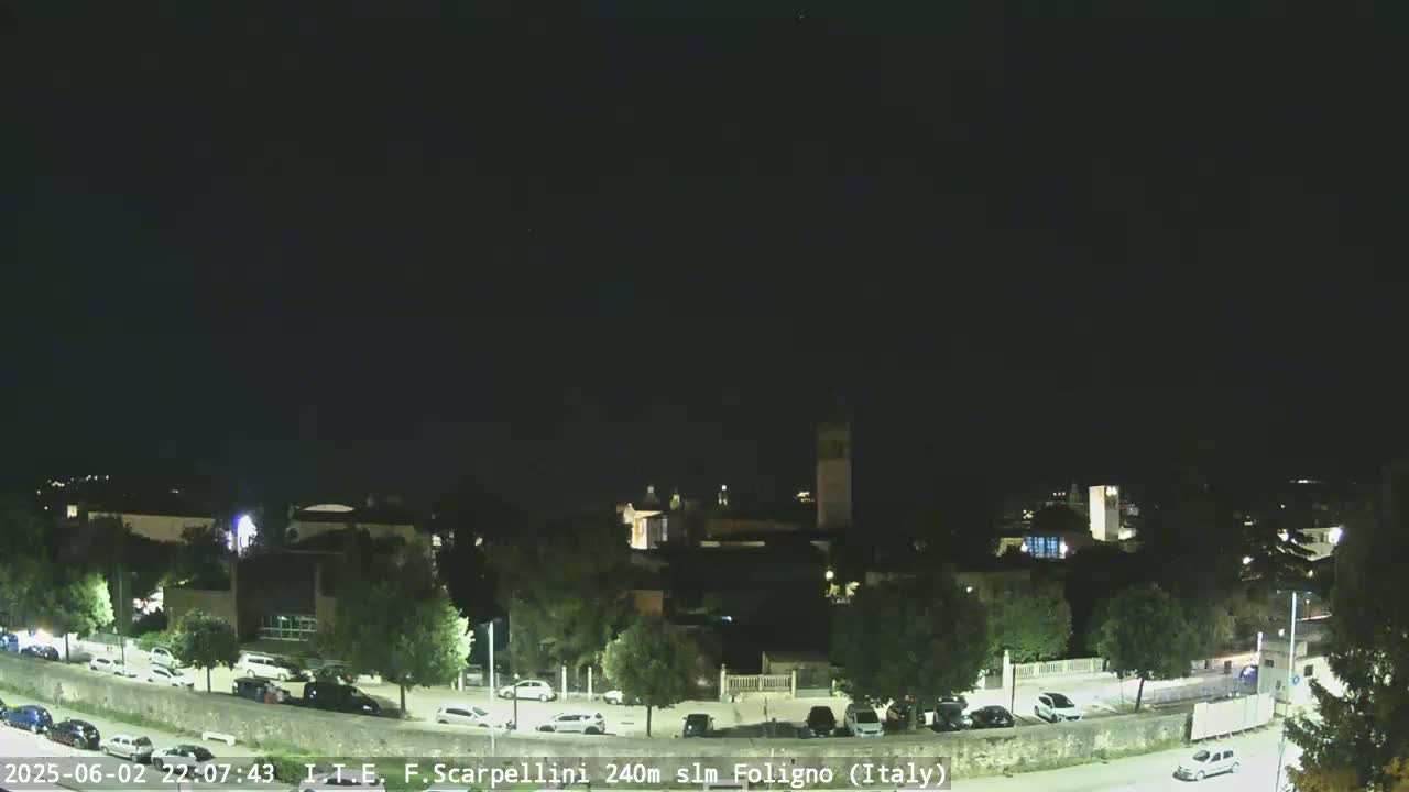 A nighttime view of a town with cars parked along a road under a clear, dark sky.