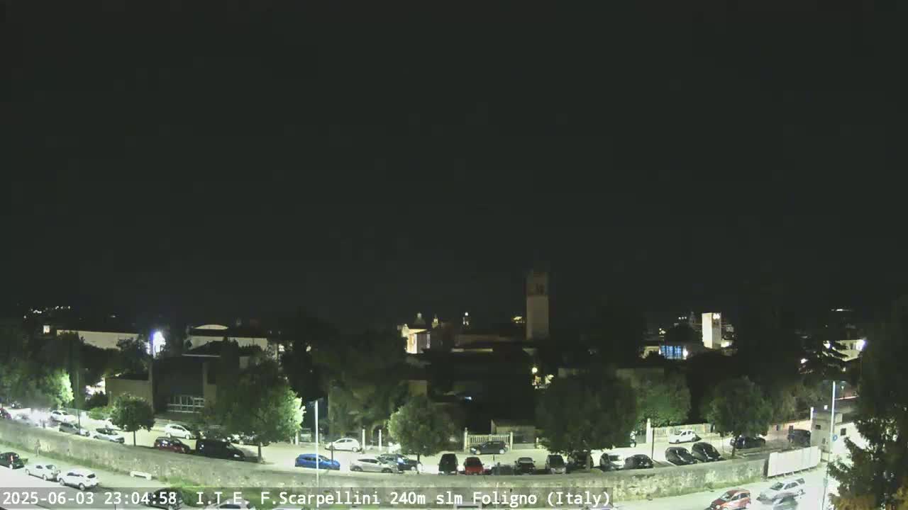 A nighttime view of a town with buildings and cars parked in a lot, under a clear, dark sky.