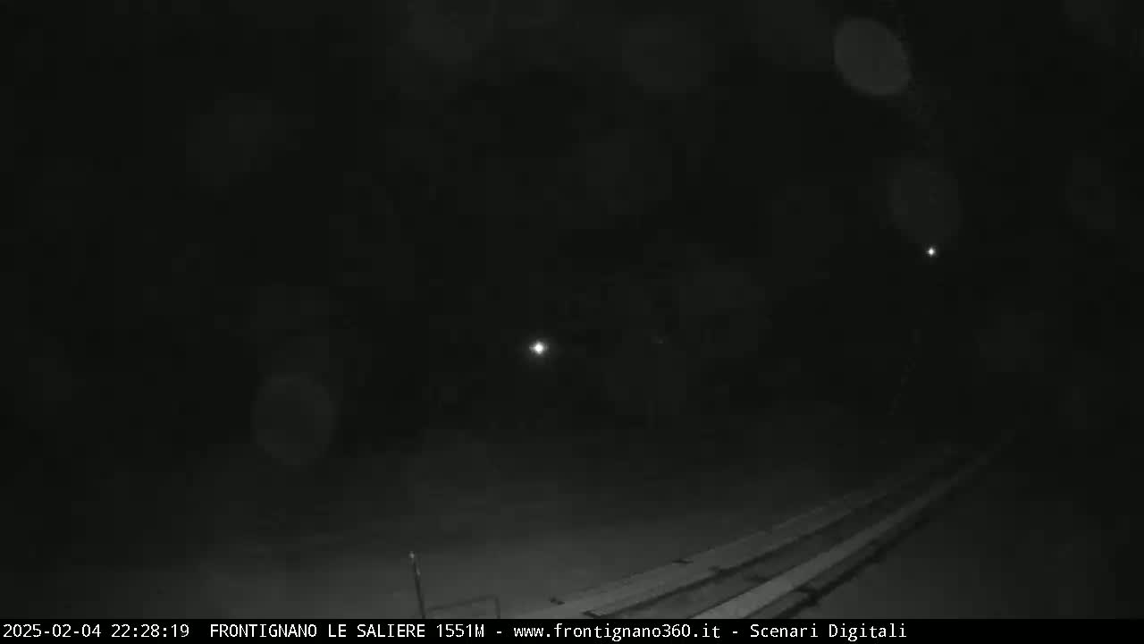 A nighttime, low-light image shows a dark, possibly outdoor scene with a faintly visible structure in the lower right corner and several small, distant lights.