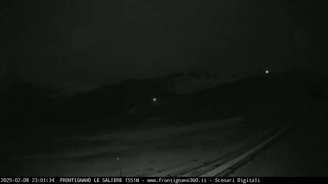 A nighttime, low-light view of a dark landscape with a few faint lights visible in the distance.