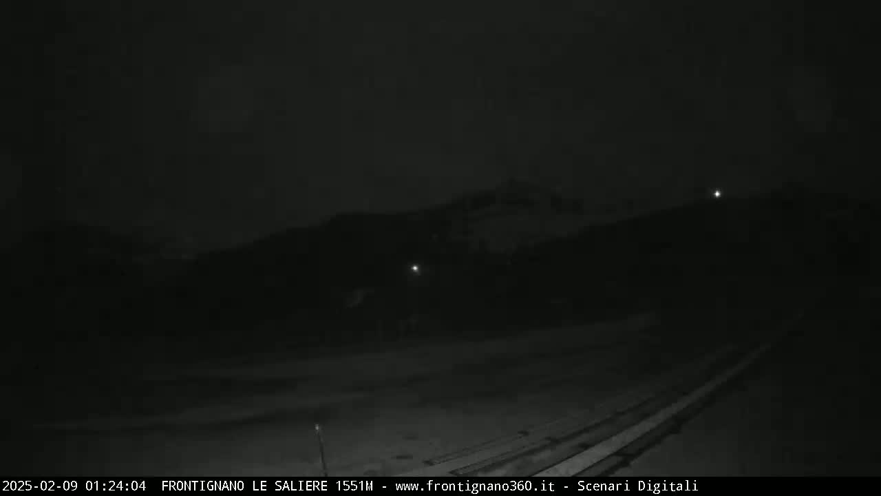 A nighttime, low-light view shows a dark landscape with faint lights in the distance.
