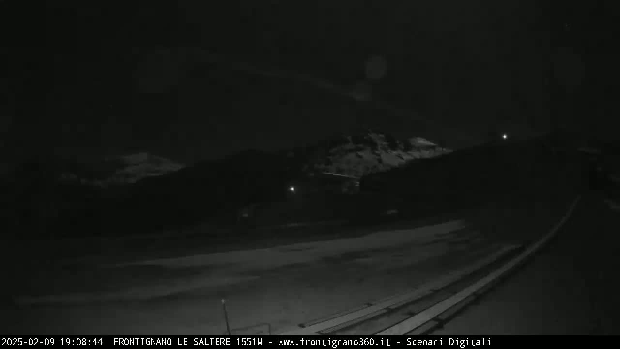 A nighttime, low-light view of a snowy, mountainous landscape, showing a long, slightly sloped surface possibly made of metal or concrete in the foreground.