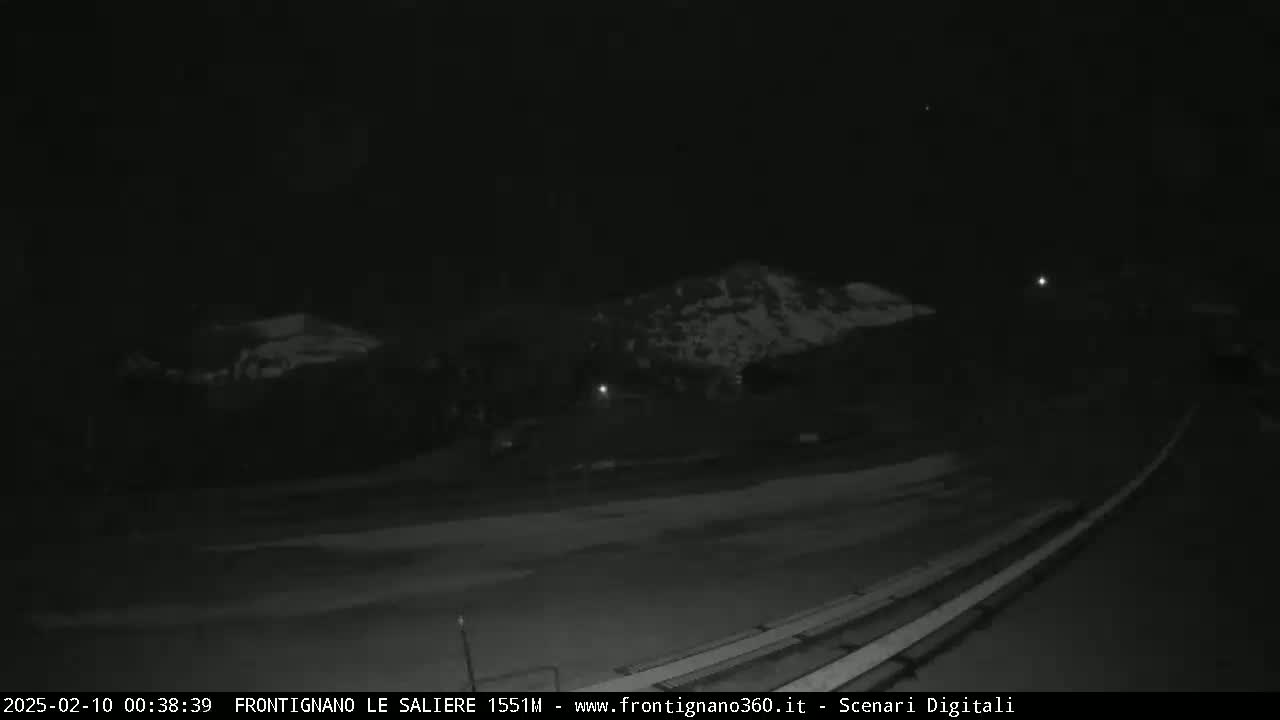 A nighttime, snow-covered hill is visible in the distance, with a long, dark structure in the foreground under a clear, dark sky.