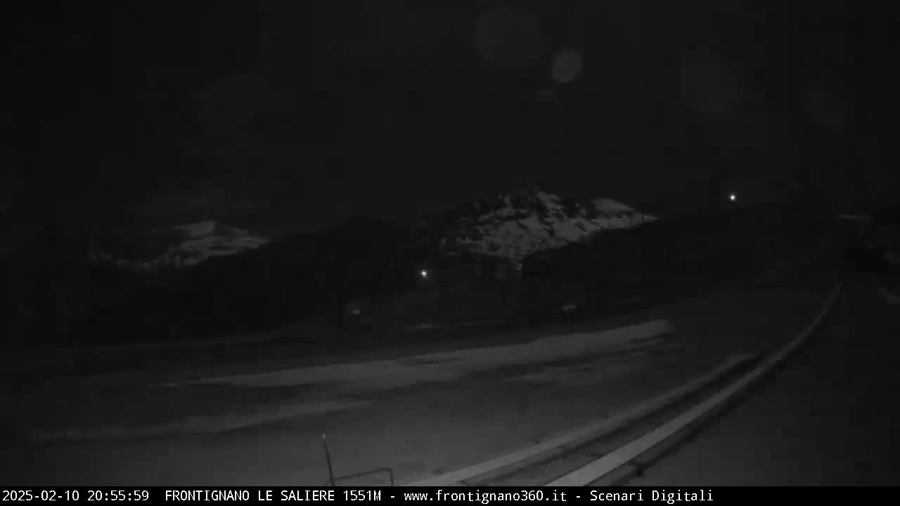 A nighttime, low-light view of a snow-covered mountain range and a road.