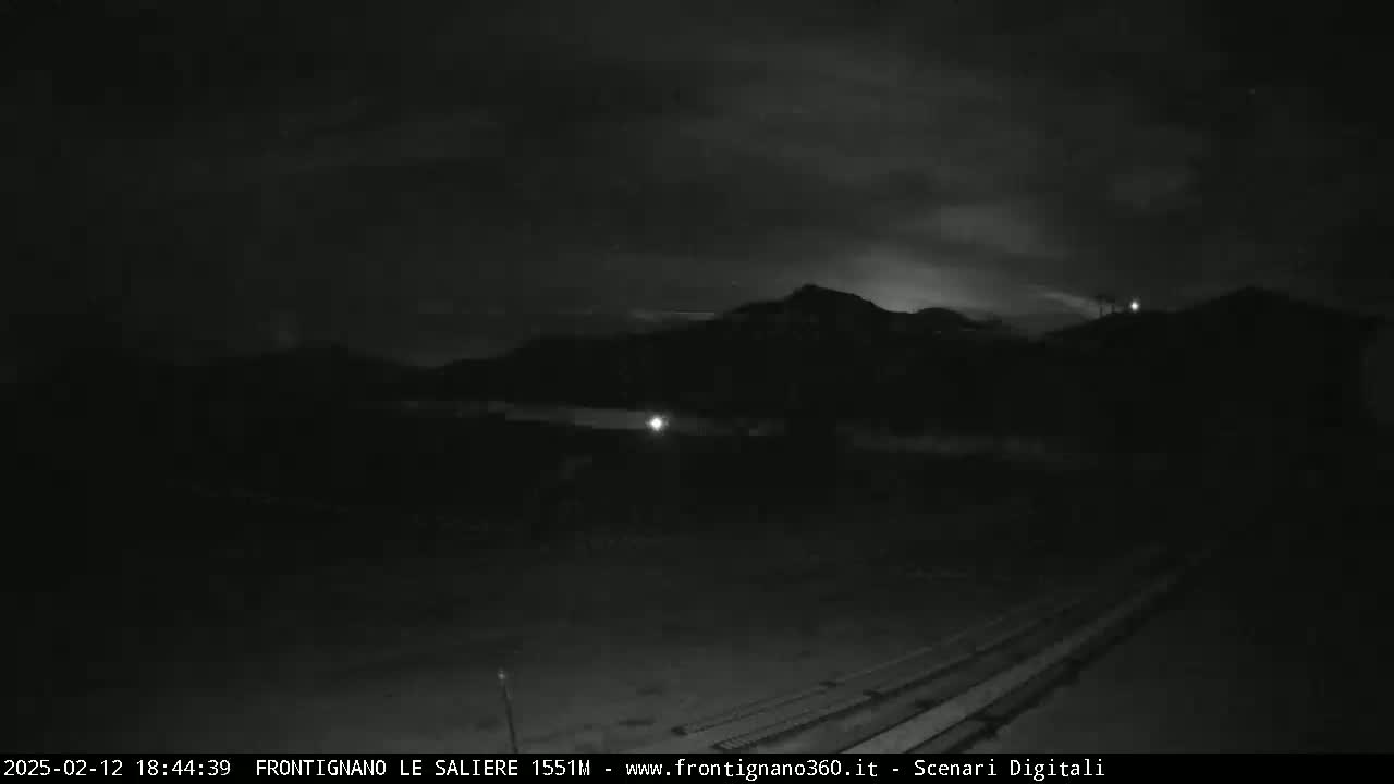 A nighttime, low-light view of a dark, mountainous landscape under a cloudy sky.