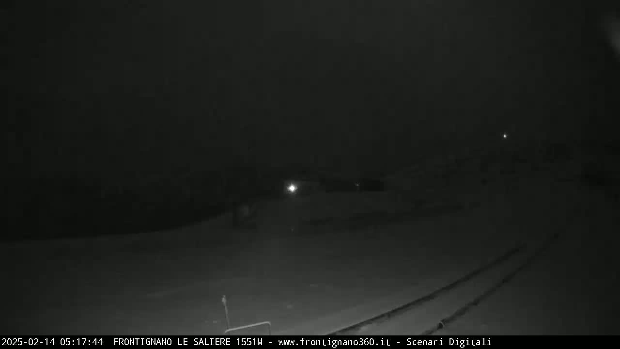A nighttime, low-light view of a snow-covered area with faint light sources in the distance.