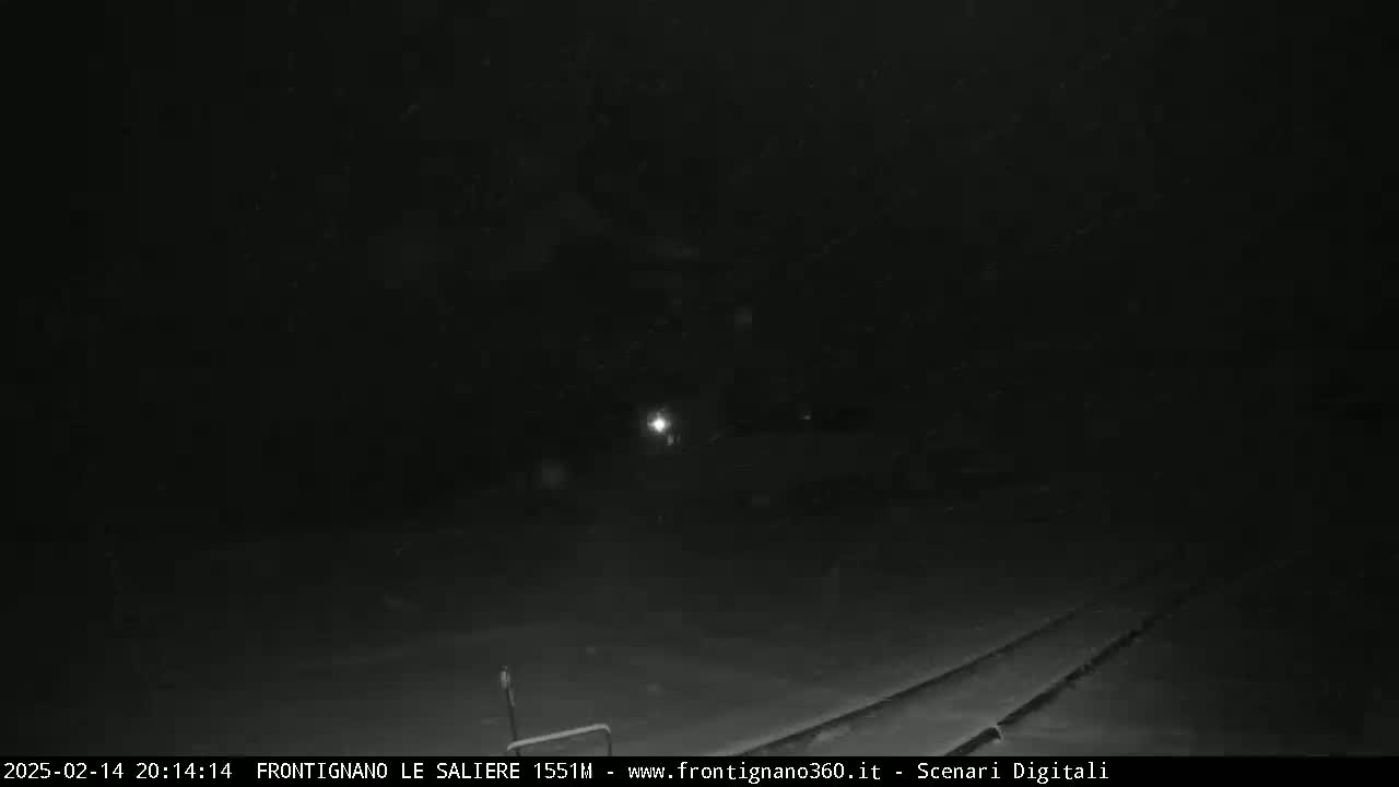 A dark, snowy nighttime scene shows a dimly lit road and faint headlights in the distance.
