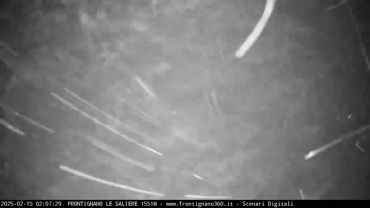 A nighttime outdoor scene shows numerous bright streaks of light moving across a dark, overcast sky.