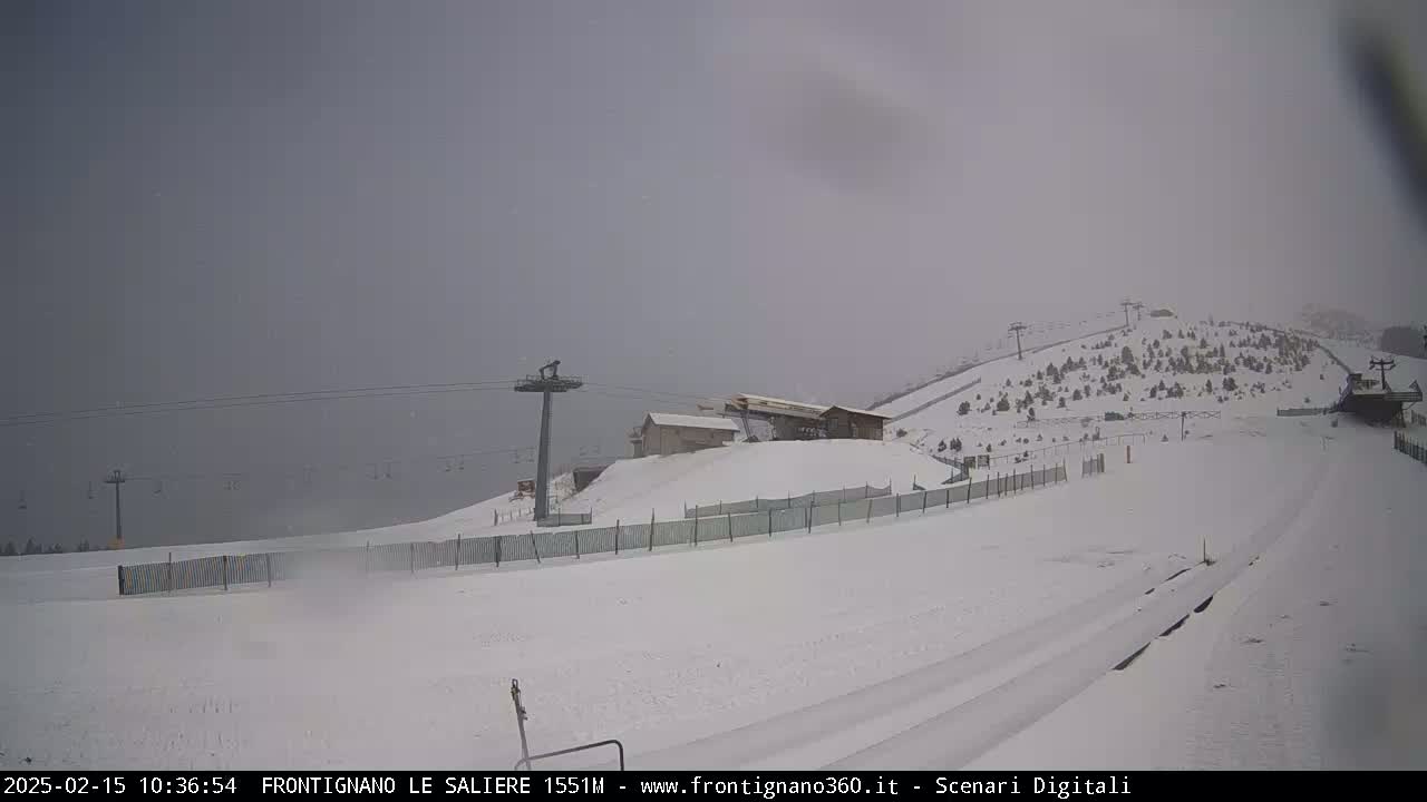 A snow-covered ski slope with chairlifts and a small building is visible under an overcast sky.