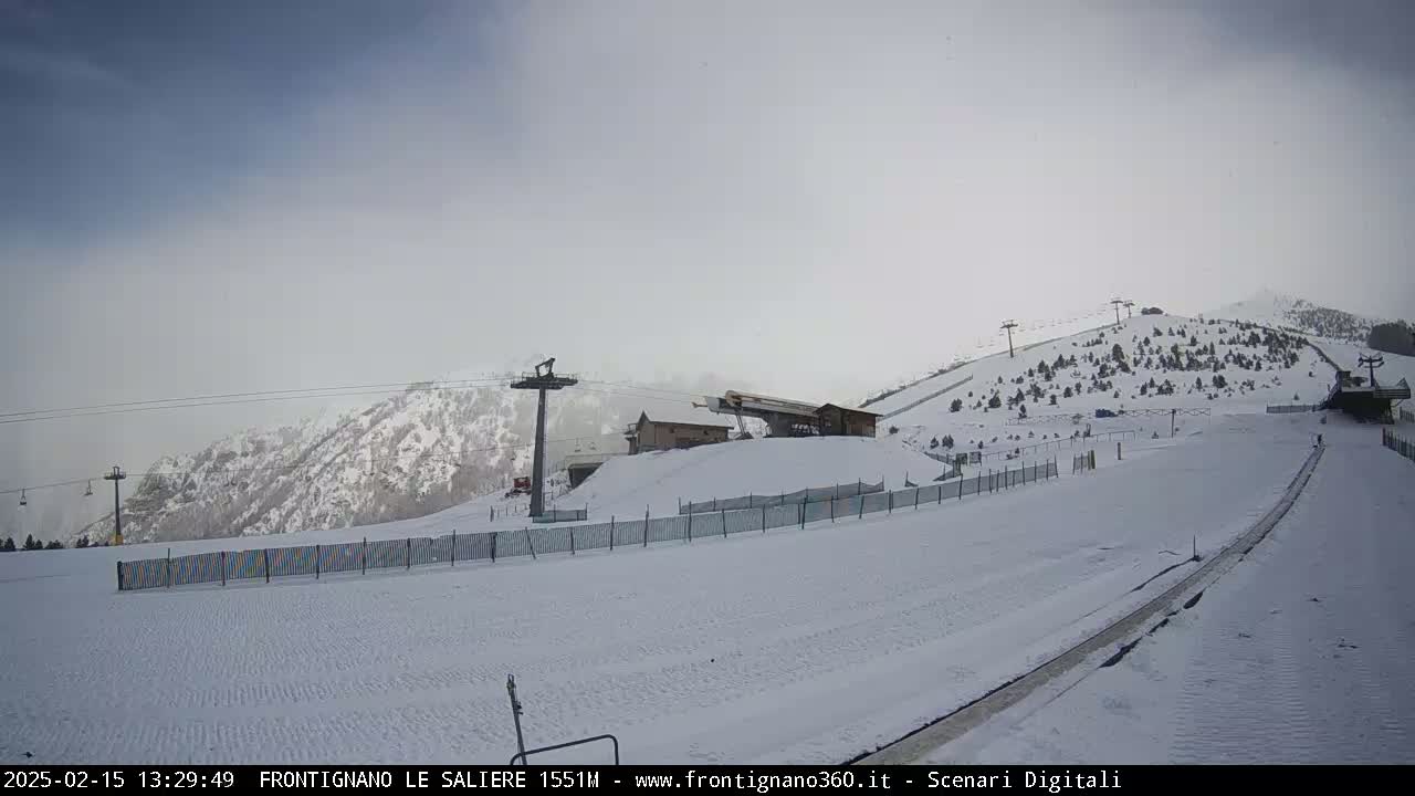 A snow-covered ski slope with ski lifts and a building under an overcast sky.