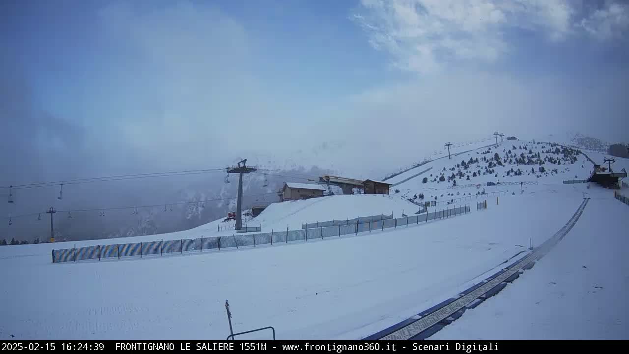 A snowy ski slope with chairlifts and a building is visible under a hazy, overcast sky.