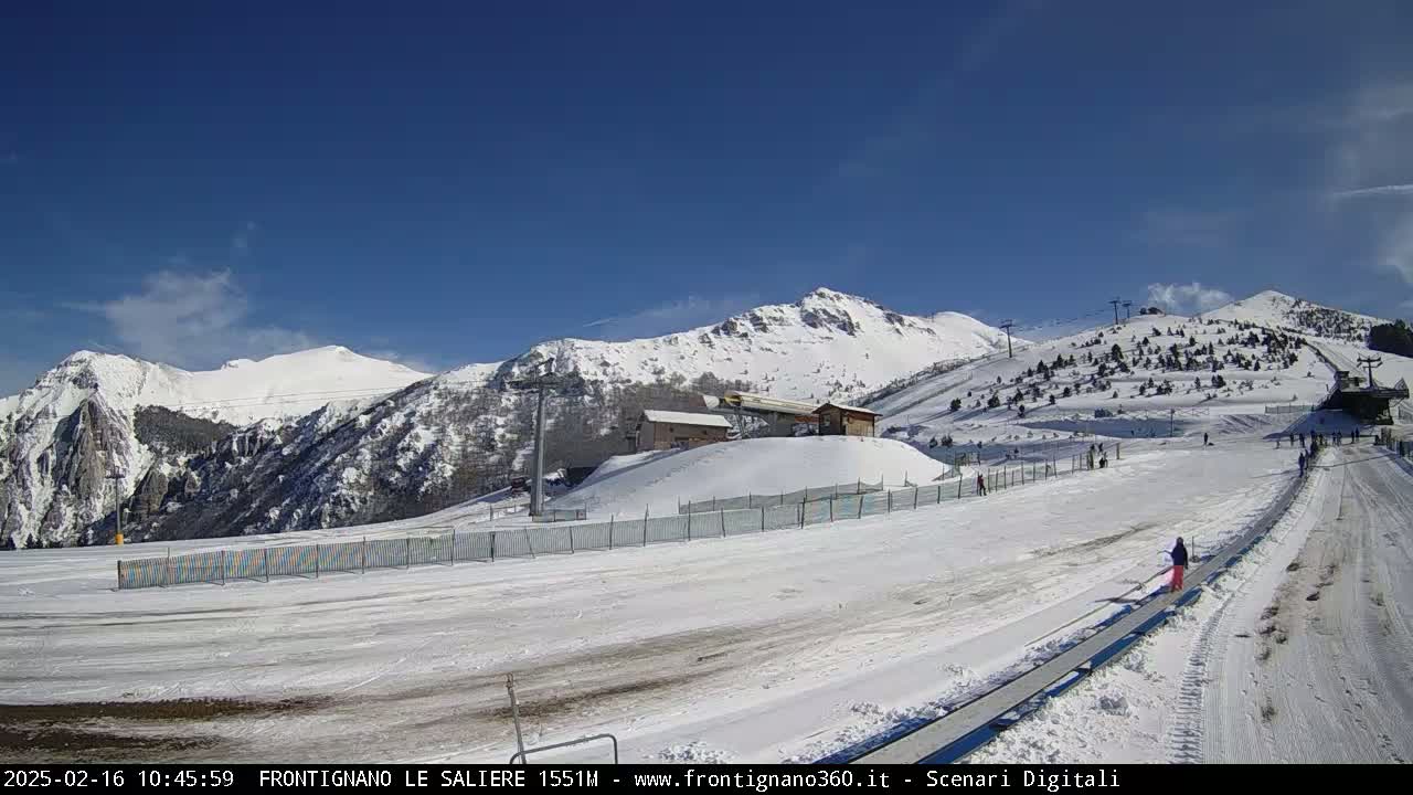 A snow-covered ski resort with mountains in the background under a clear blue sky.
