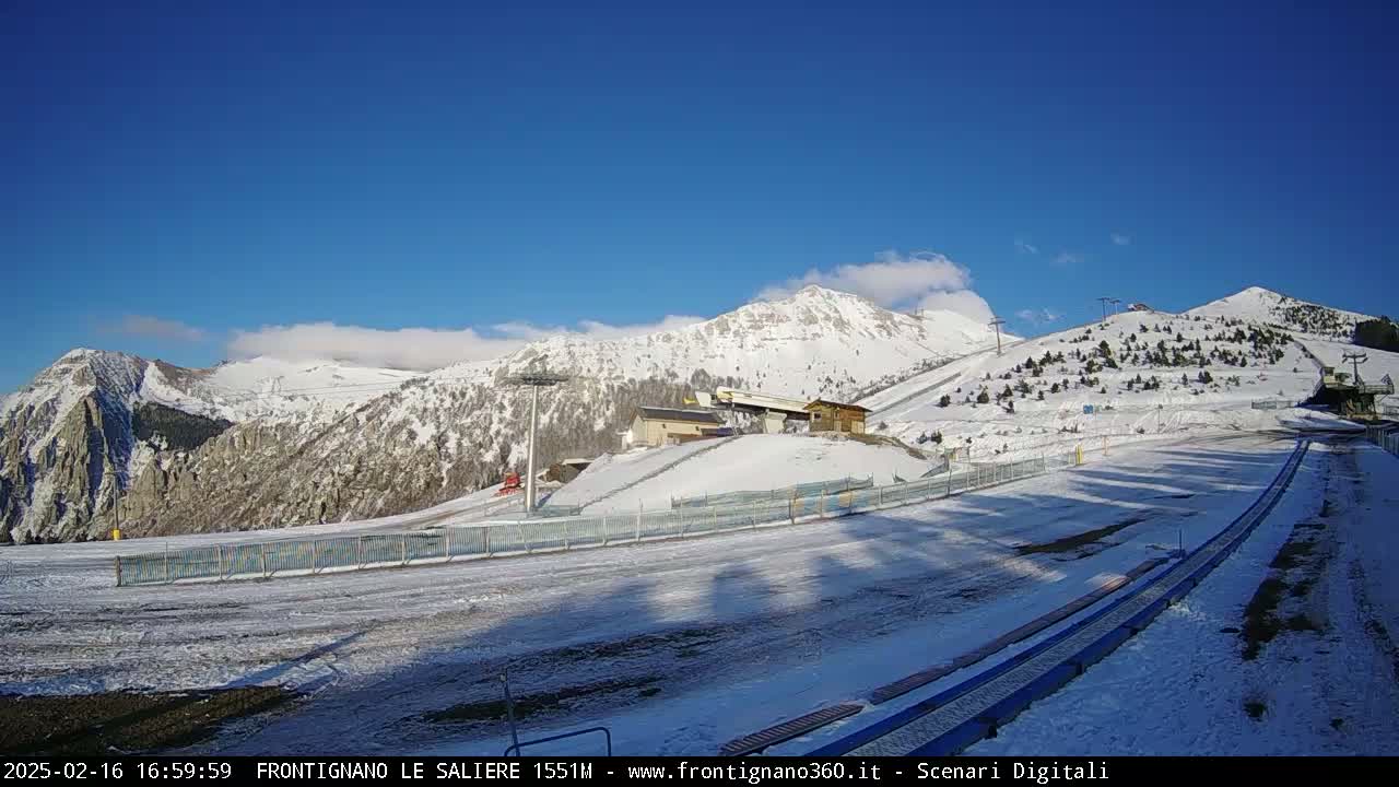 A snow-covered ski resort is situated in a mountainous area under a clear blue sky with a few clouds.