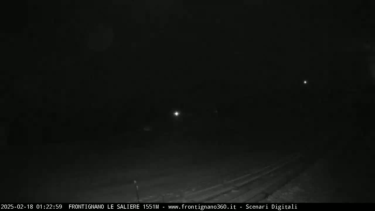 A dark, nighttime scene shows a road with faint lights in the distance.
