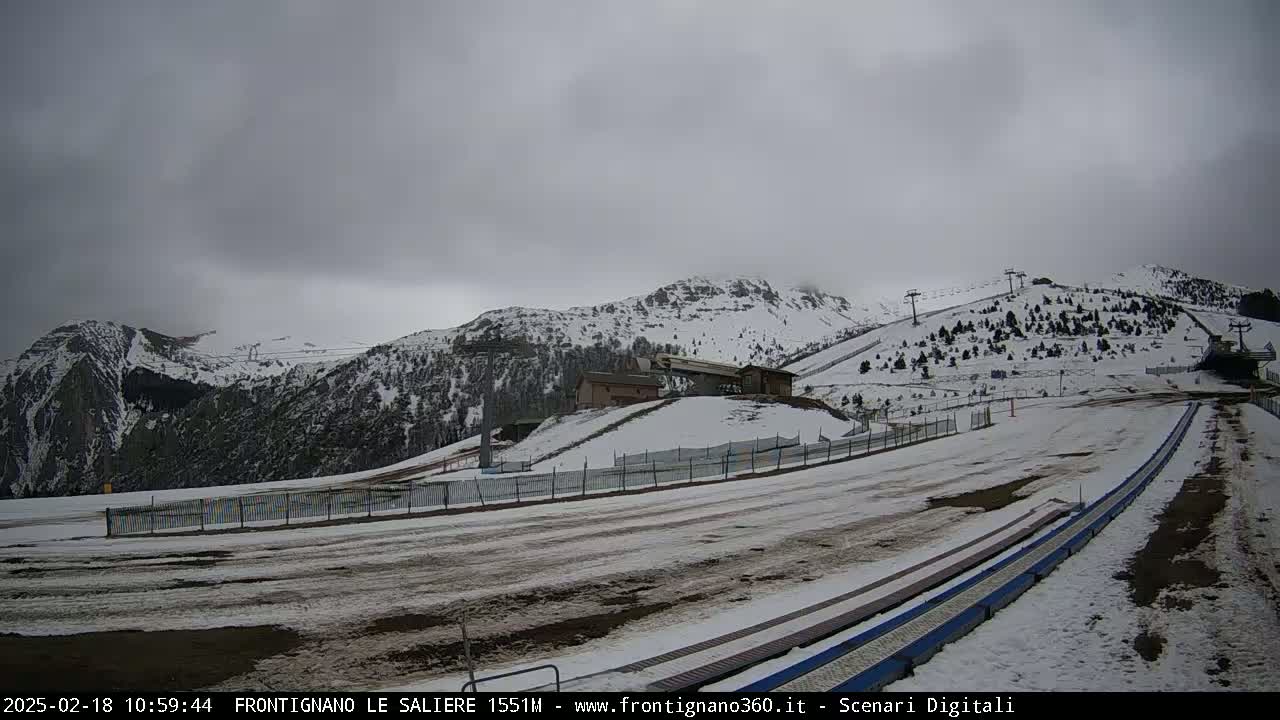A snow-covered mountain landscape with ski lifts and a building under an overcast sky.