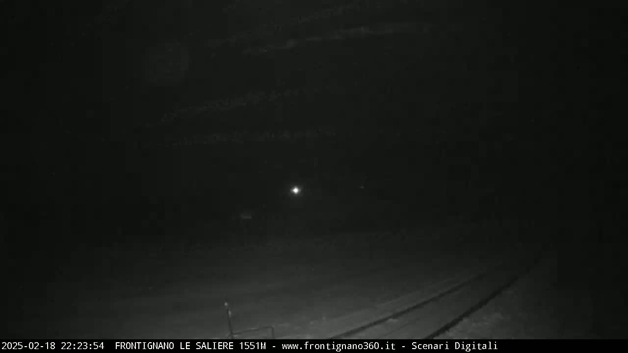 A dark, nighttime scene shows a dimly lit roadway with faint tire tracks and a single distant light source.