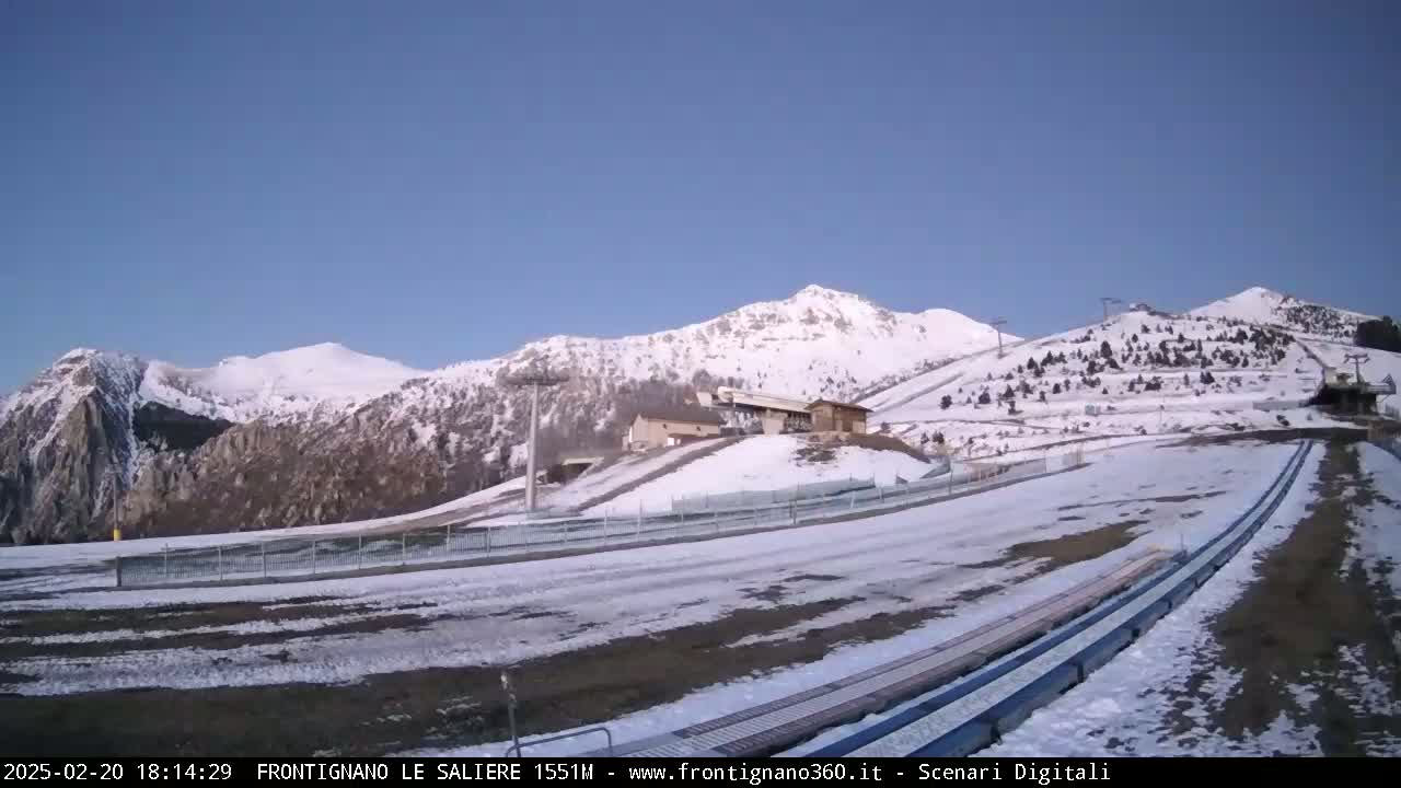 A snow-covered mountain landscape with ski lifts and runs, under a clear blue sky.