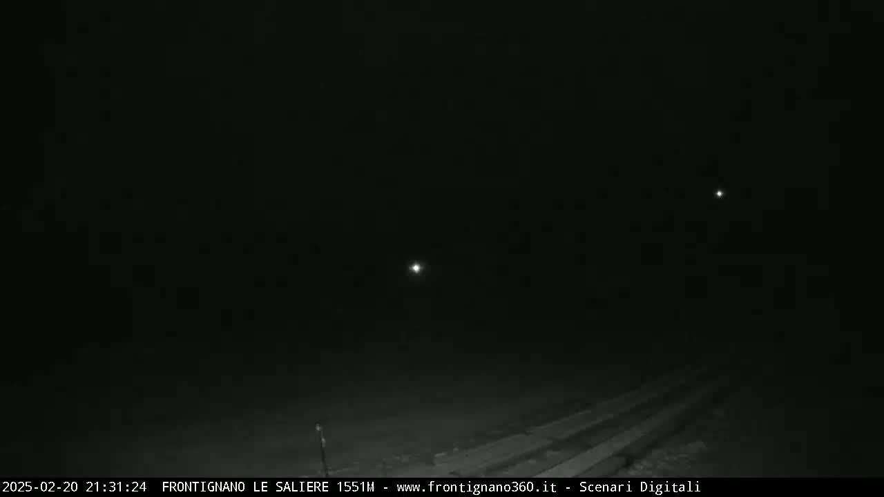 A dark, nighttime scene shows a road with faint light sources in the distance.