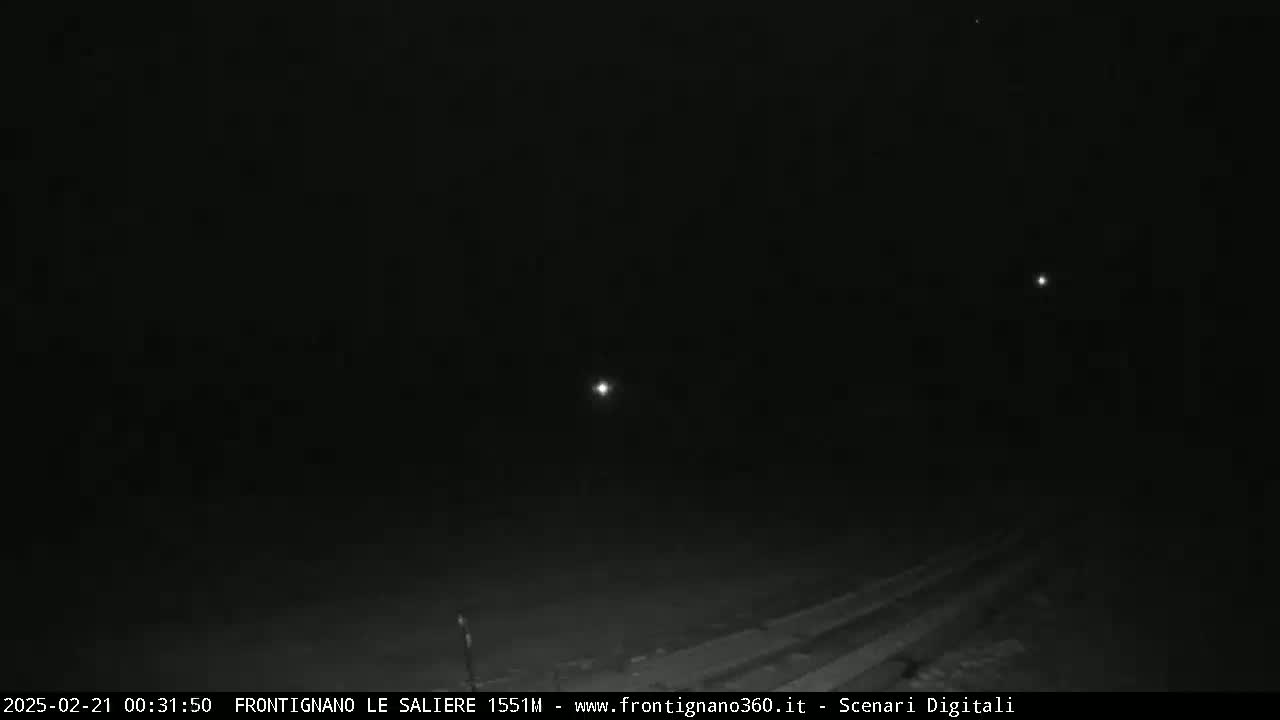 A dark, nighttime scene shows a road with a few distant lights visible under a clear sky.