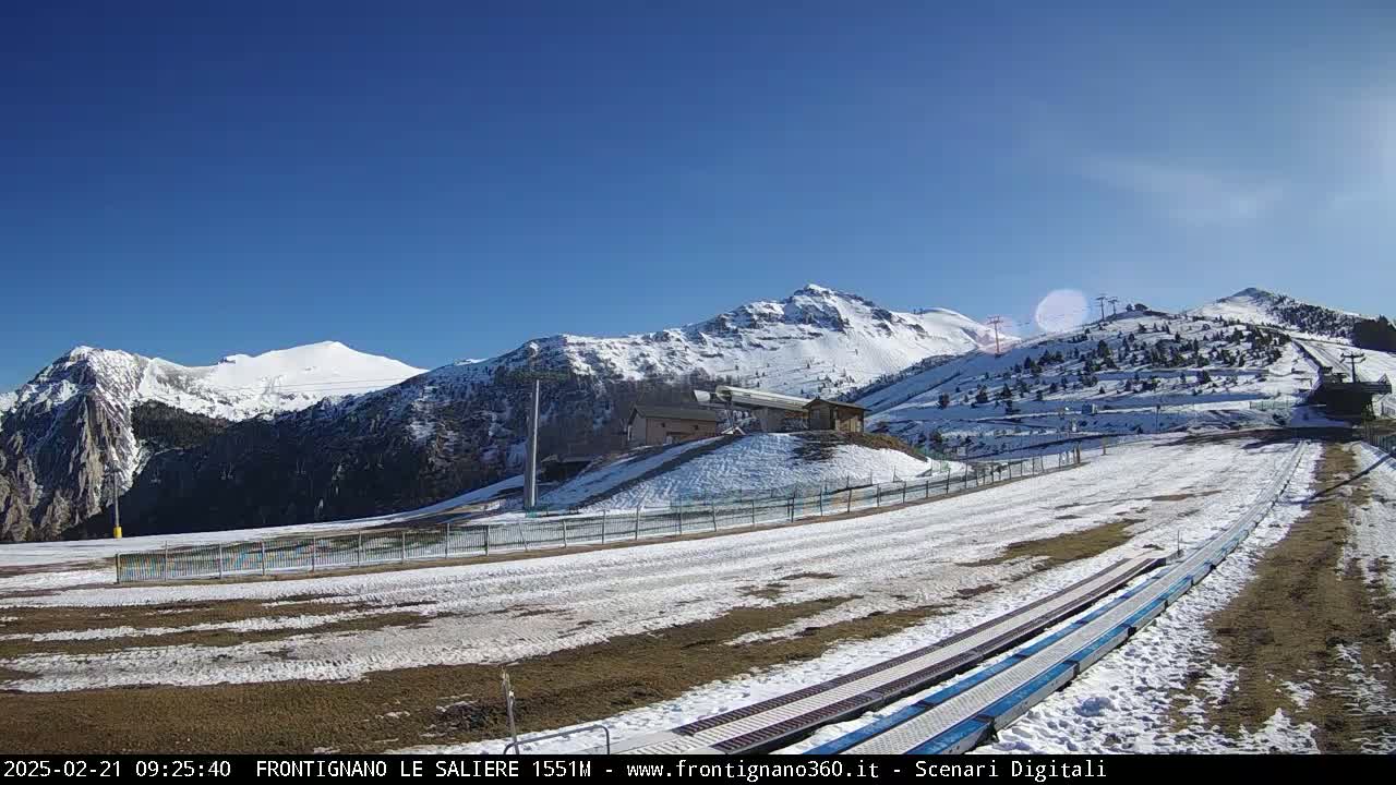 A sunny, snow-covered mountain landscape with ski lifts and a snow-covered path leading to them.