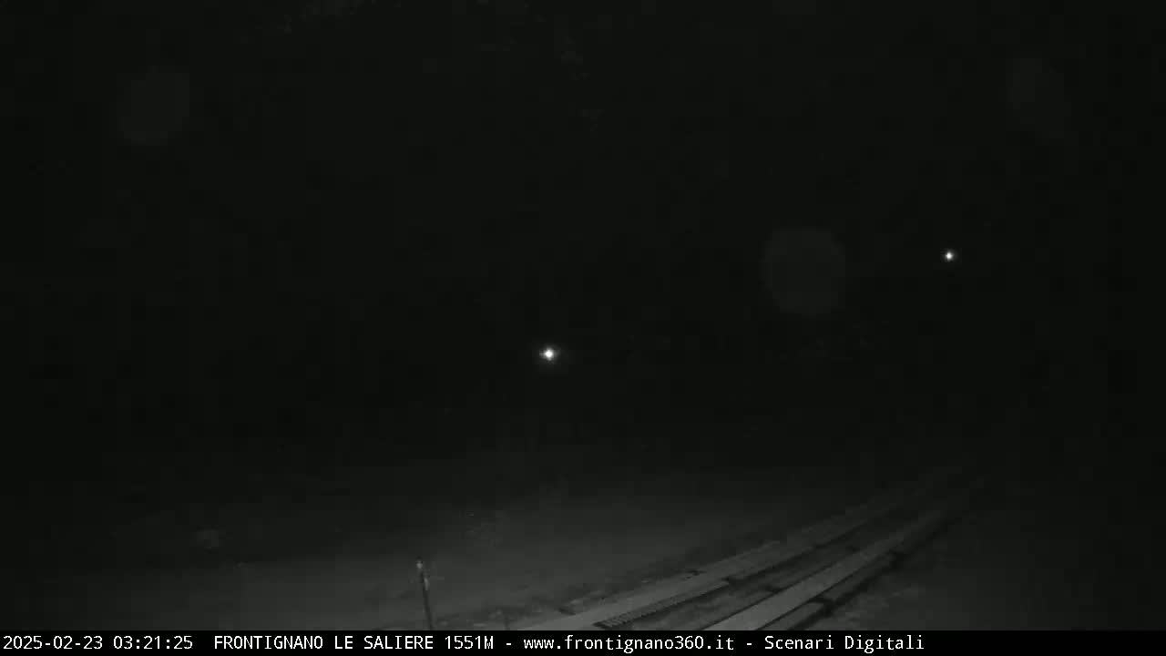 A nighttime, low-light image shows a dark area with a few distant lights and a section of what appears to be wooden planks in the foreground.