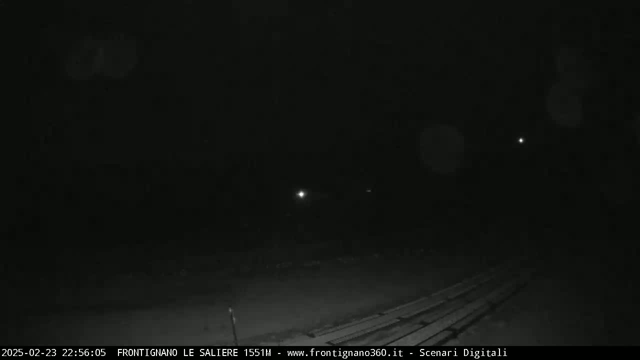 A nighttime, low-light view shows a dark, empty area with a few distant lights and what appears to be a wooden structure or planks in the lower right corner.