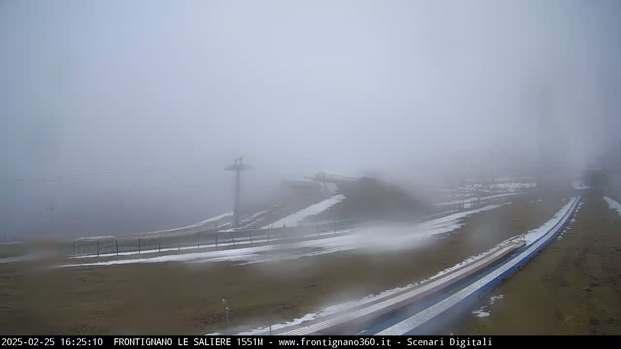 A foggy, snowy landscape shows a ski slope with a chairlift and snow-covered ground.