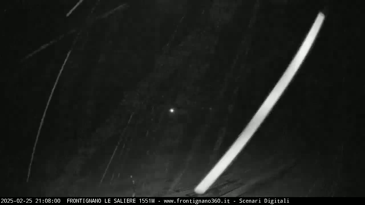 A nighttime outdoor scene shows streaks of light, possibly from rain or snow, and two bright diagonal lines across a dark sky.