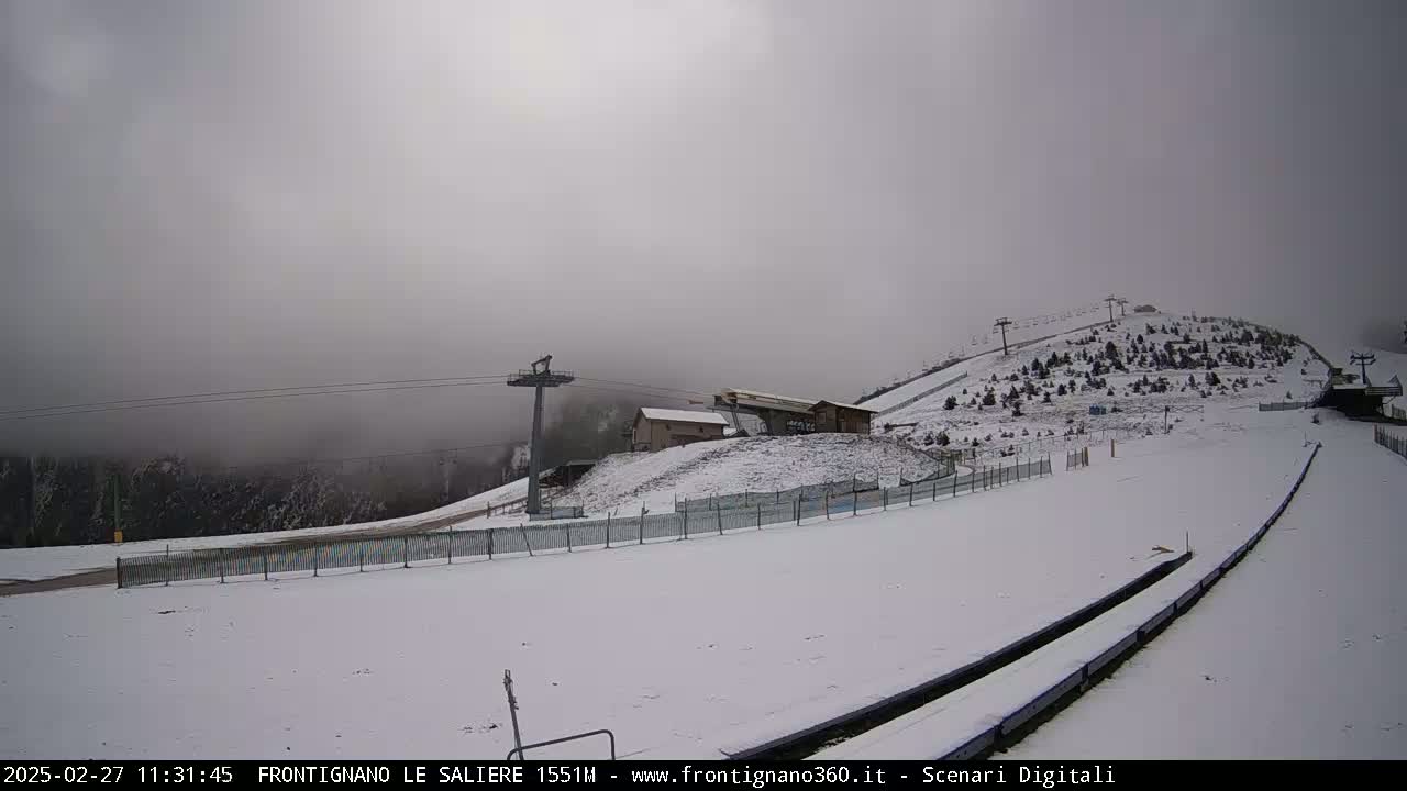 A snow-covered ski slope with chairlifts and a foggy sky.