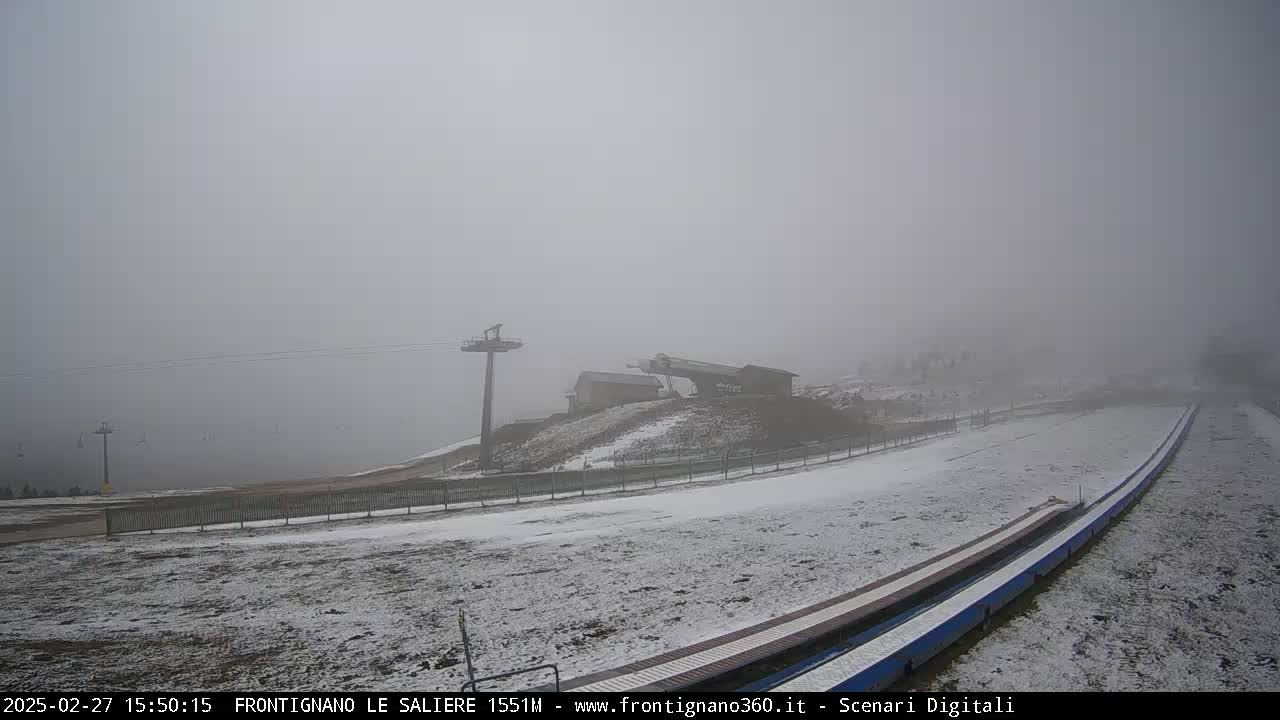 A snow-dusted ski slope and lift station are shrouded in thick fog.